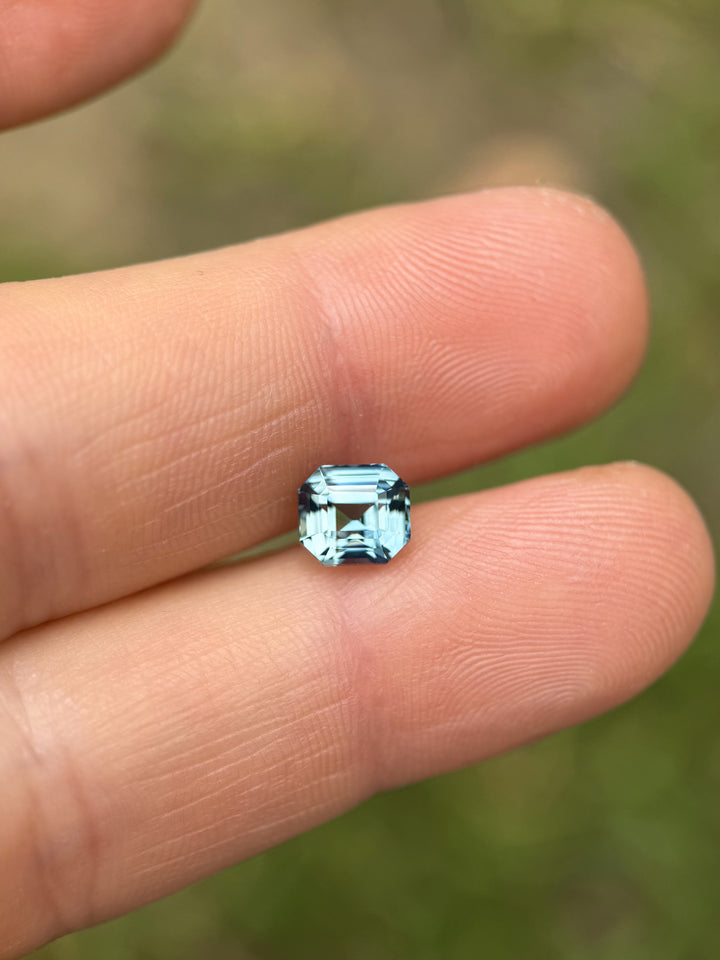 Hand holding a 2.14-carat unheated sky blue sapphire from Madagascar in an emerald cut, showing its clarity and step-cut brilliance.