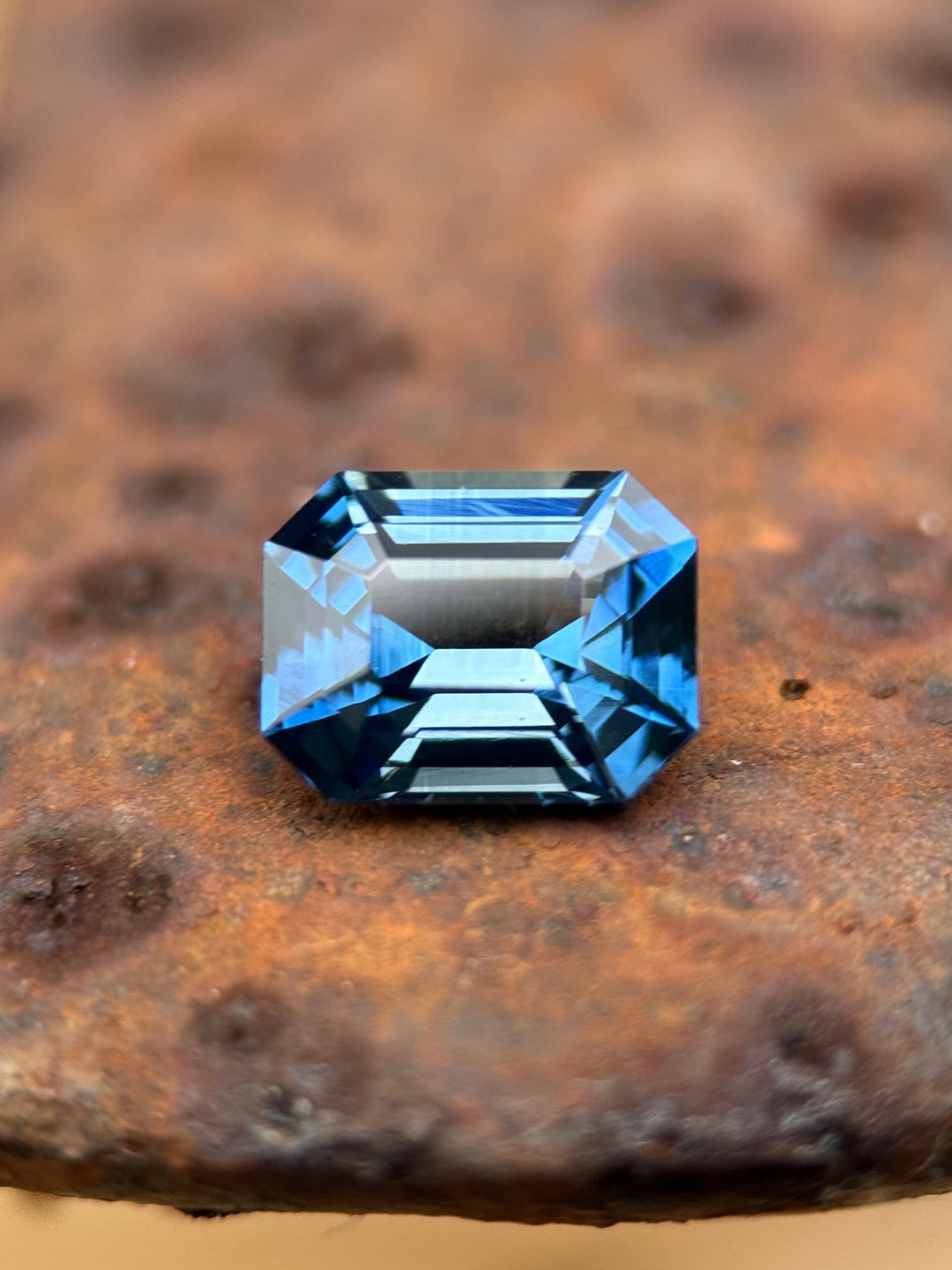 Loose vivid teal indigo blue sapphire emerald cut on textured surface showing step facets and deep saturation, natural gemstone.
