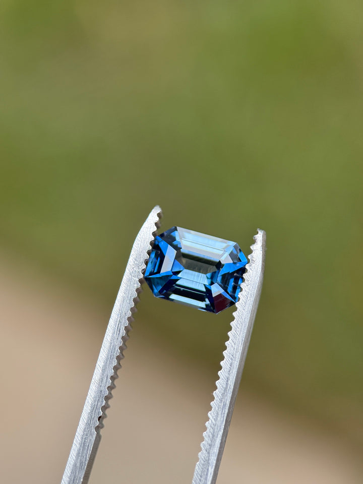 2.14 carat teal blue sapphire emerald cut held in tweezers highlighting precision cut, symmetry, and rich color depth.