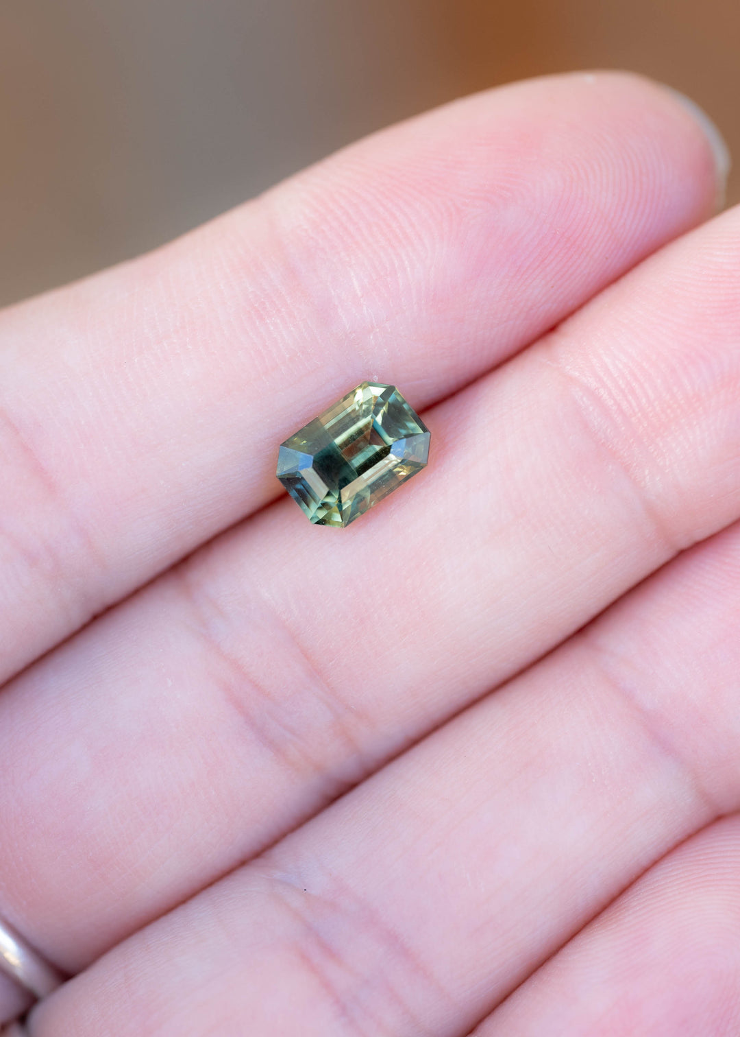 Untreated 2.16ct yellow teal green parti sapphire photographed on fingers to demonstrate its size, elongated octagonal shape and natural multicolor appearance.