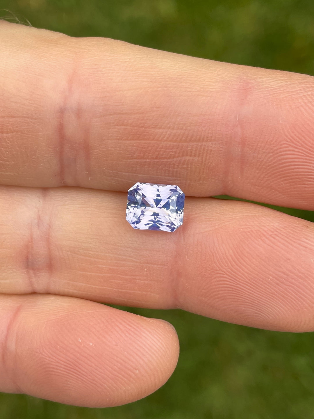 Hand-held view of a 2.16-carat custom radiant cut sapphire in peach, lavender, and violet hues from Sri Lanka, unheated and ethically sourced.