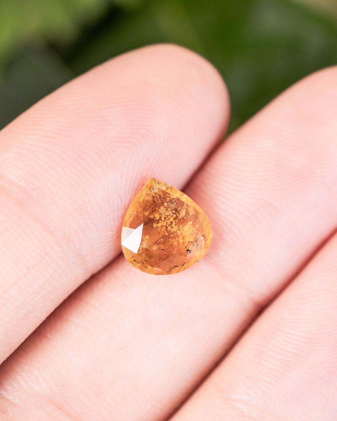 2.17 carat sapphire with Dijon mustard and banana nut yellow hues resting on a fingertip, showcasing warm orange reflections and natural inclusions in a custom wide pear cut, untreated gemstone from Umba River, Tanzania.