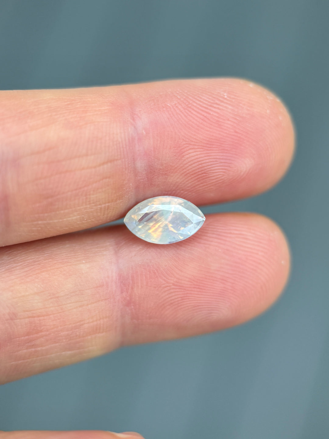 2.18 carat opalescent peach and gray sapphire shown on fingertip under daylight, displaying its natural color transitions and craftsmanship in a precision marquise mixed cut, untreated sapphire from Ratnapura, Sri Lanka.