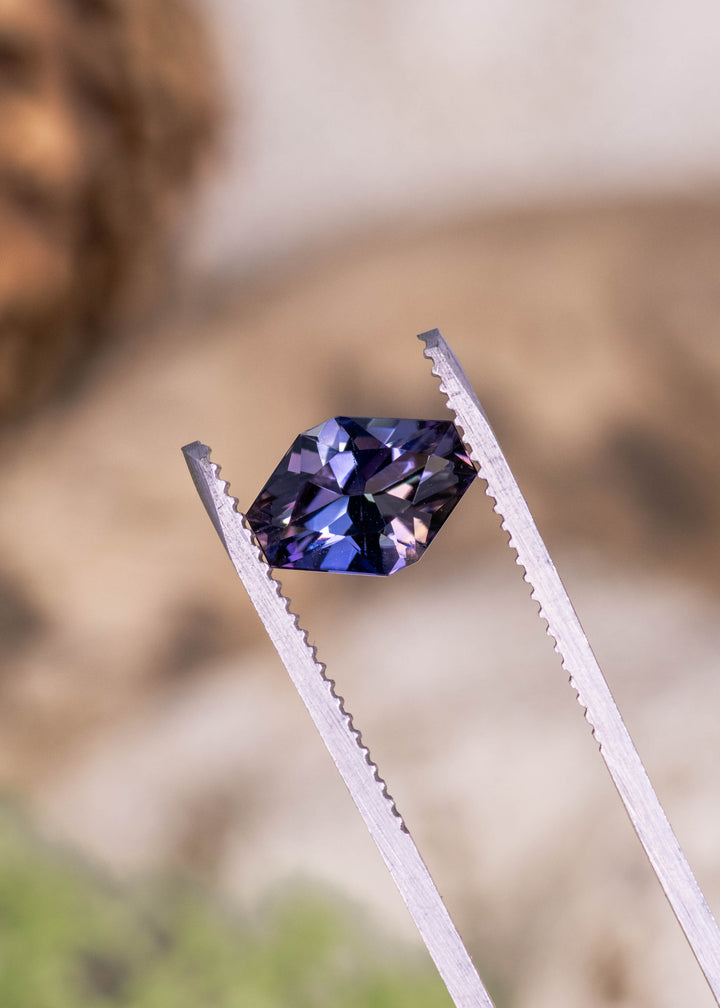 2.19 carat peach lavender blue purple Tanzanite geometric asymmetrical octagon held in tweezers, precision faceted gemstone from Merelani Hills Arusha Tanzania displaying sharp angular facets, electric blue flashes and designer cut symmetry for fine jewelry