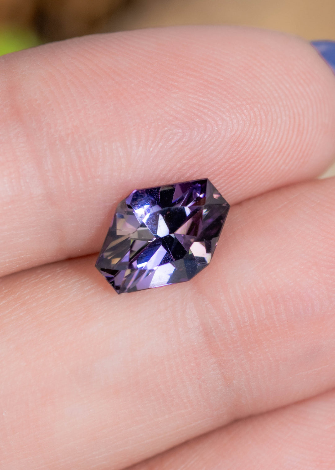2.19 carat peach lavender blue purple Tanzanite resting on finger, custom geometric asymmetrical octagon cut gemstone from Tanzania highlighting crisp facet junctions, vibrant brilliance and modern custom jewelry appeal