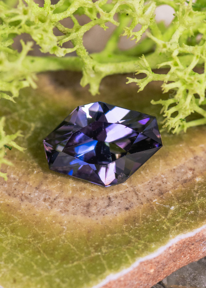 2.19 carat peach lavender blue purple Tanzanite custom geometric asymmetrical octagon displayed on natural stone surface, Merelani Hills Tanzania gemstone showing angular precision faceting, vivid color zoning and brilliant light return for custom jewelry