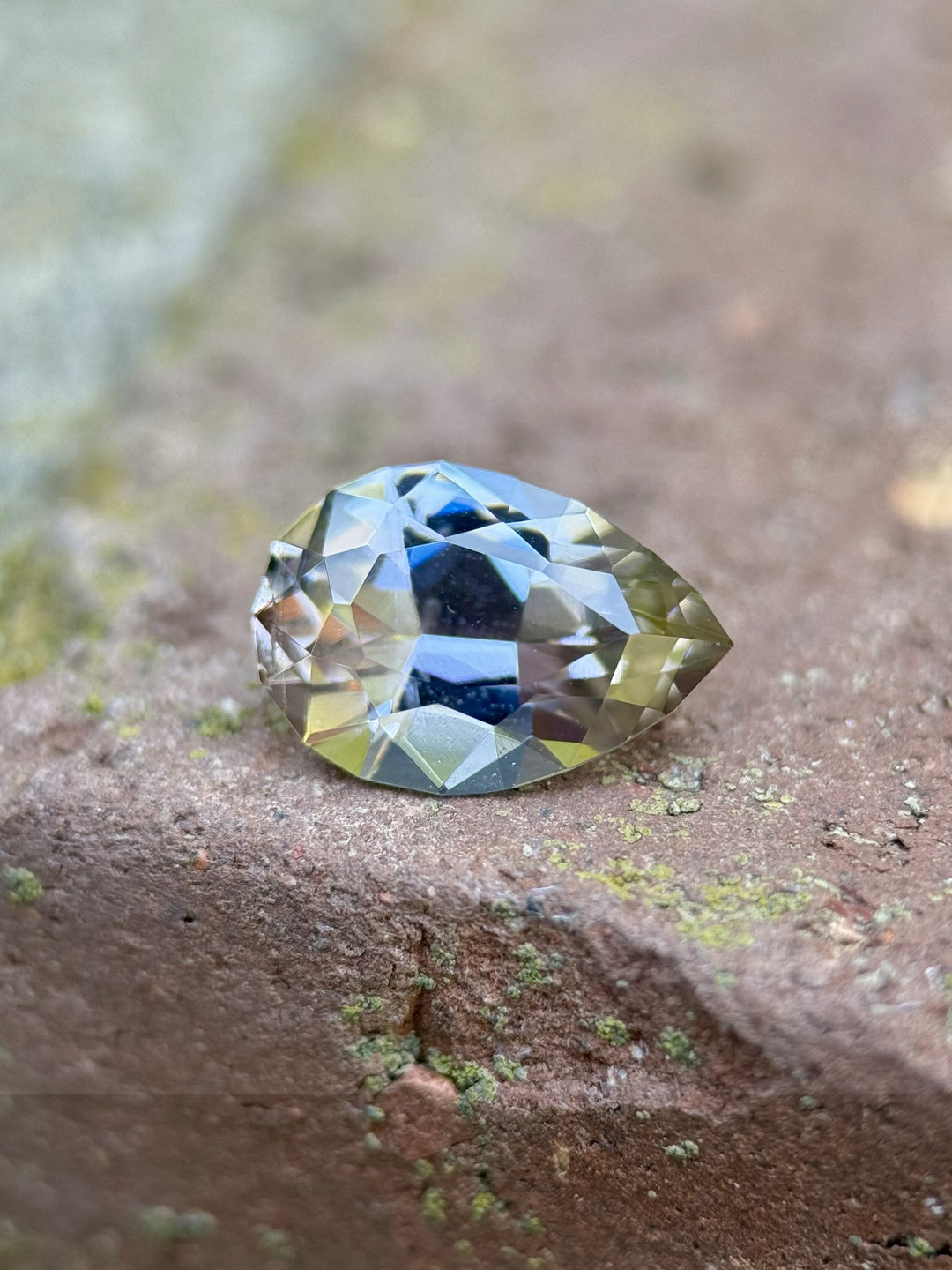 2.19 carat Tanzanite gemstone in pear mixed cut showing soft peach and blue tones, photographed on a textured brick background