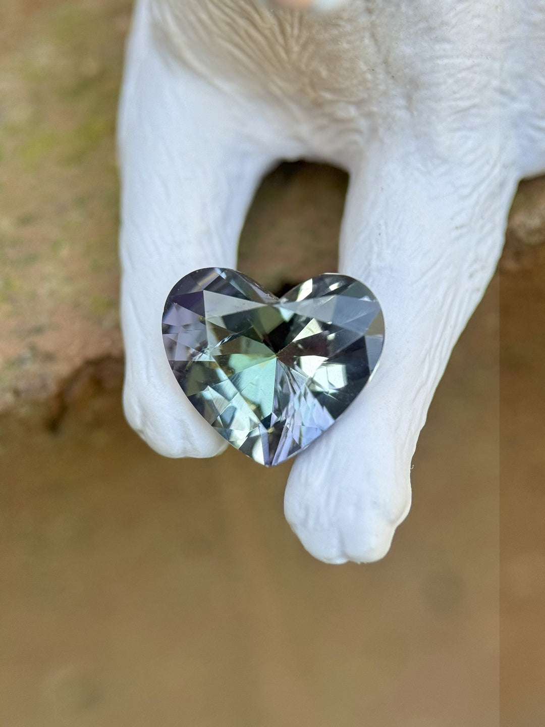 Heart-shaped 2.20 carat Tanzanite gemstone with blue, green, and lavender hues resting on white ceramic paws