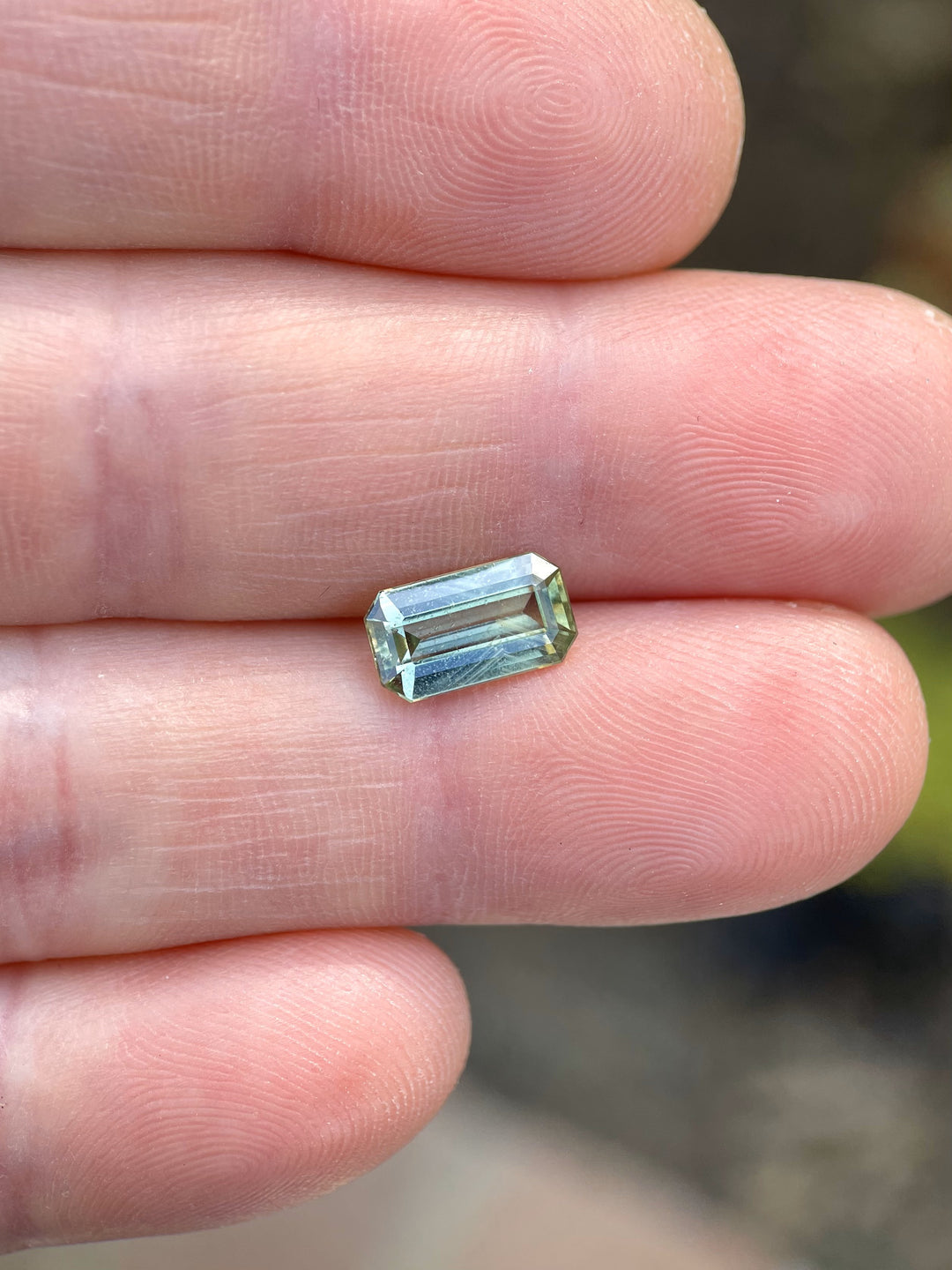 Hand holding a 2.24-carat sapphire with yellow, teal, and green hues in a modified emerald cut from Umba River, Tanzania.