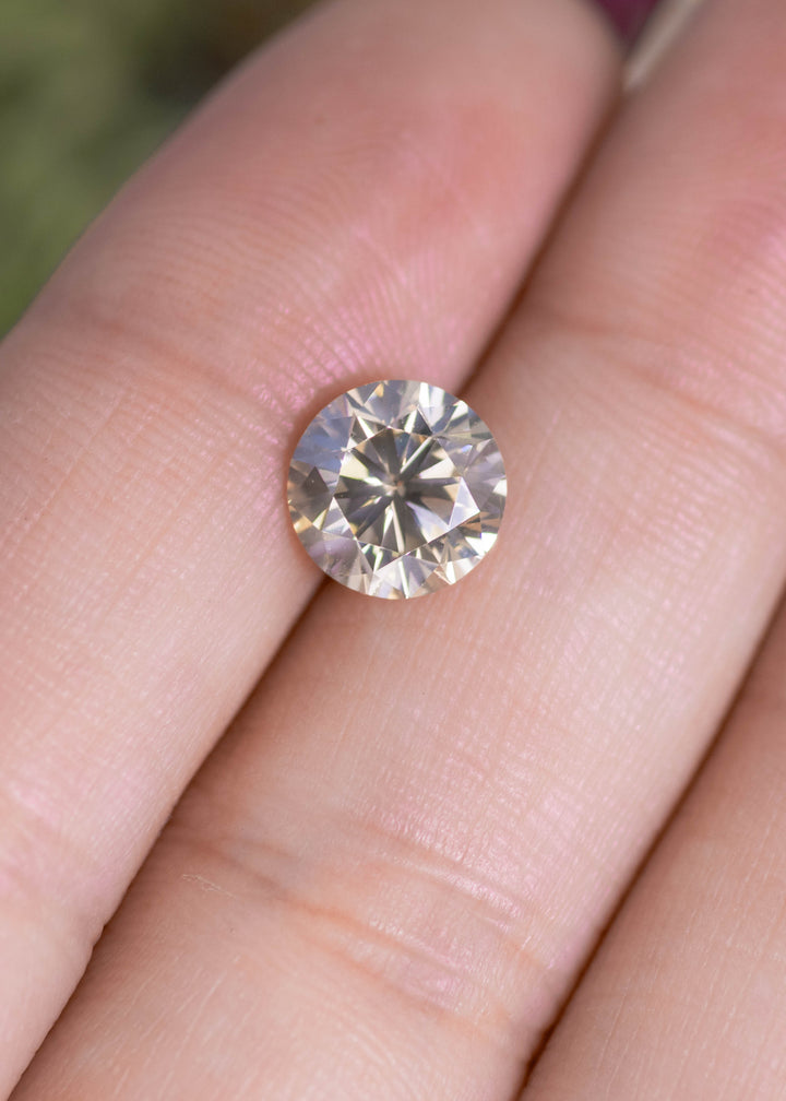 Loose 2.25 carat fancy yellow brown diamond VVS1 resting on fingertips showing round brilliant cut and champagne tone.
