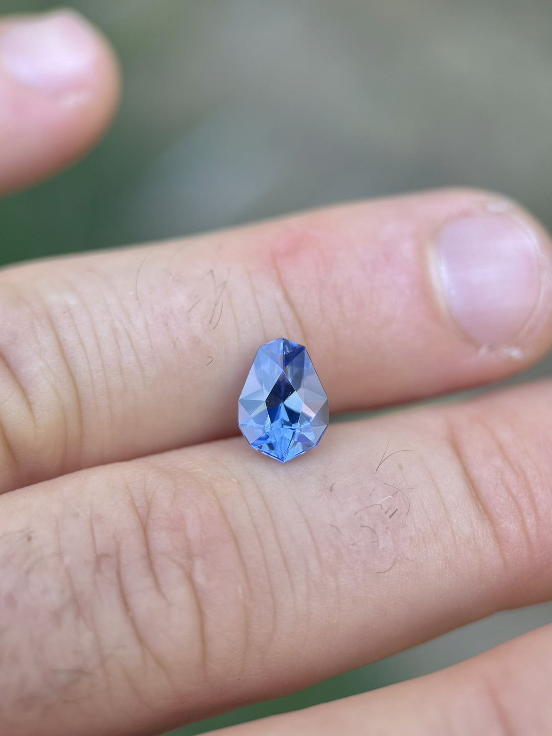 Ultra Violet Blue Tanzanite resting on fingers for scale, featuring clean facets, excellent symmetry, and vibrant color saturation.