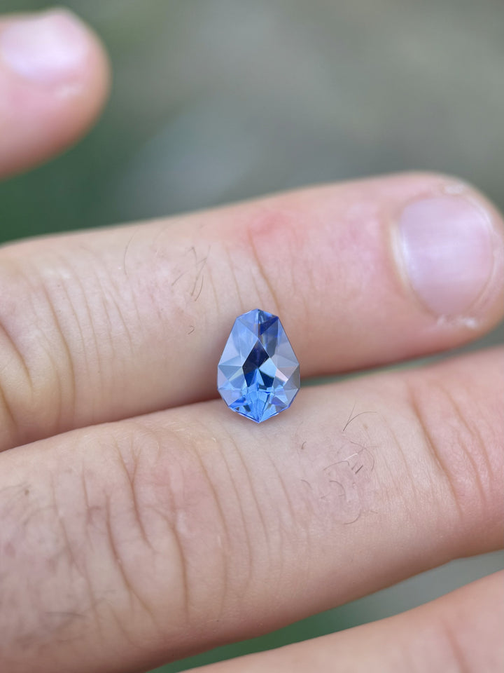 Ultra Violet Blue Tanzanite resting on fingers for scale, featuring clean facets, excellent symmetry, and vibrant color saturation.