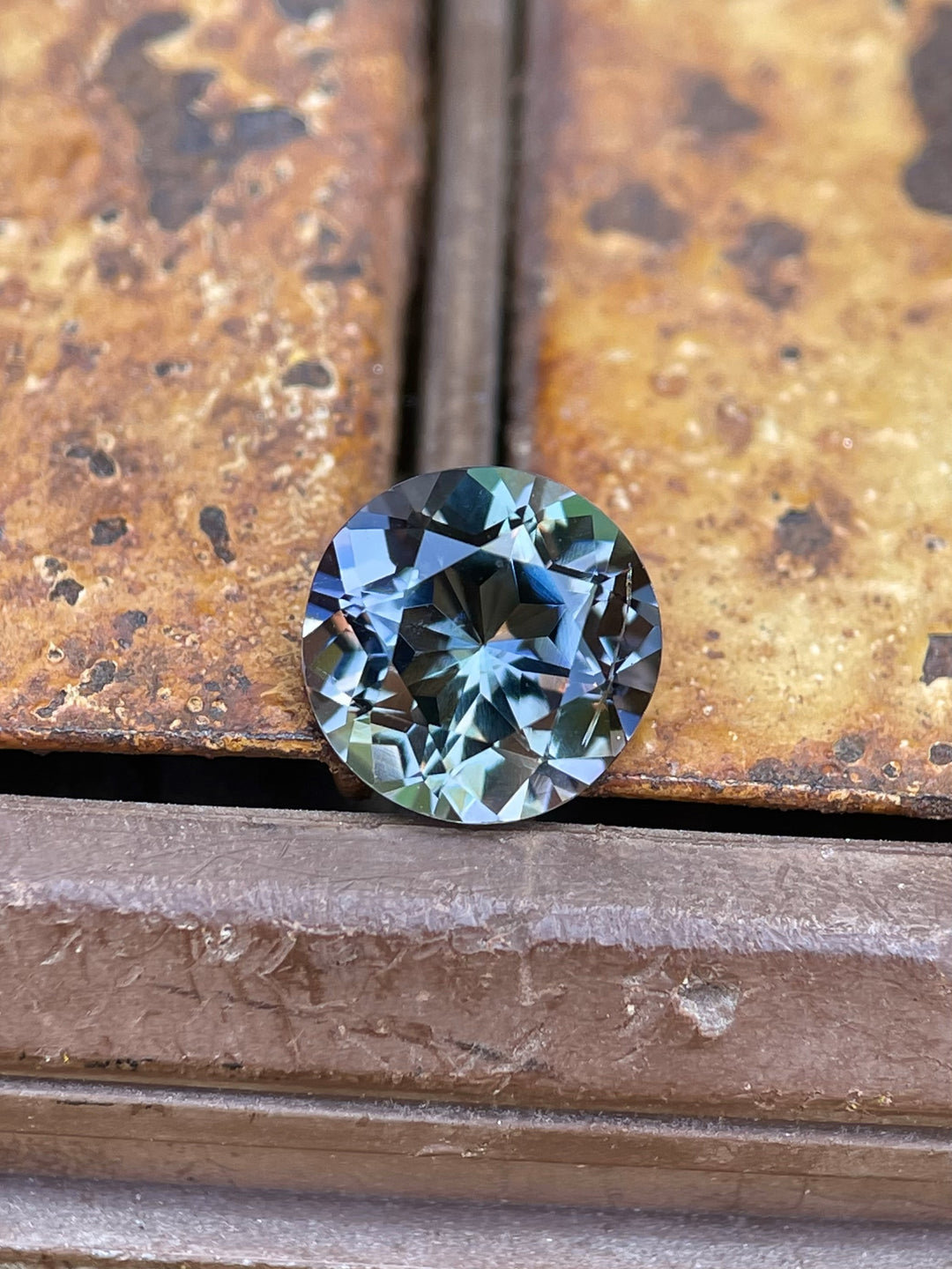 Round-cut 2.26-carat Tanzanite gemstone showcasing teal, purple, and blue hues on a rustic metal surface