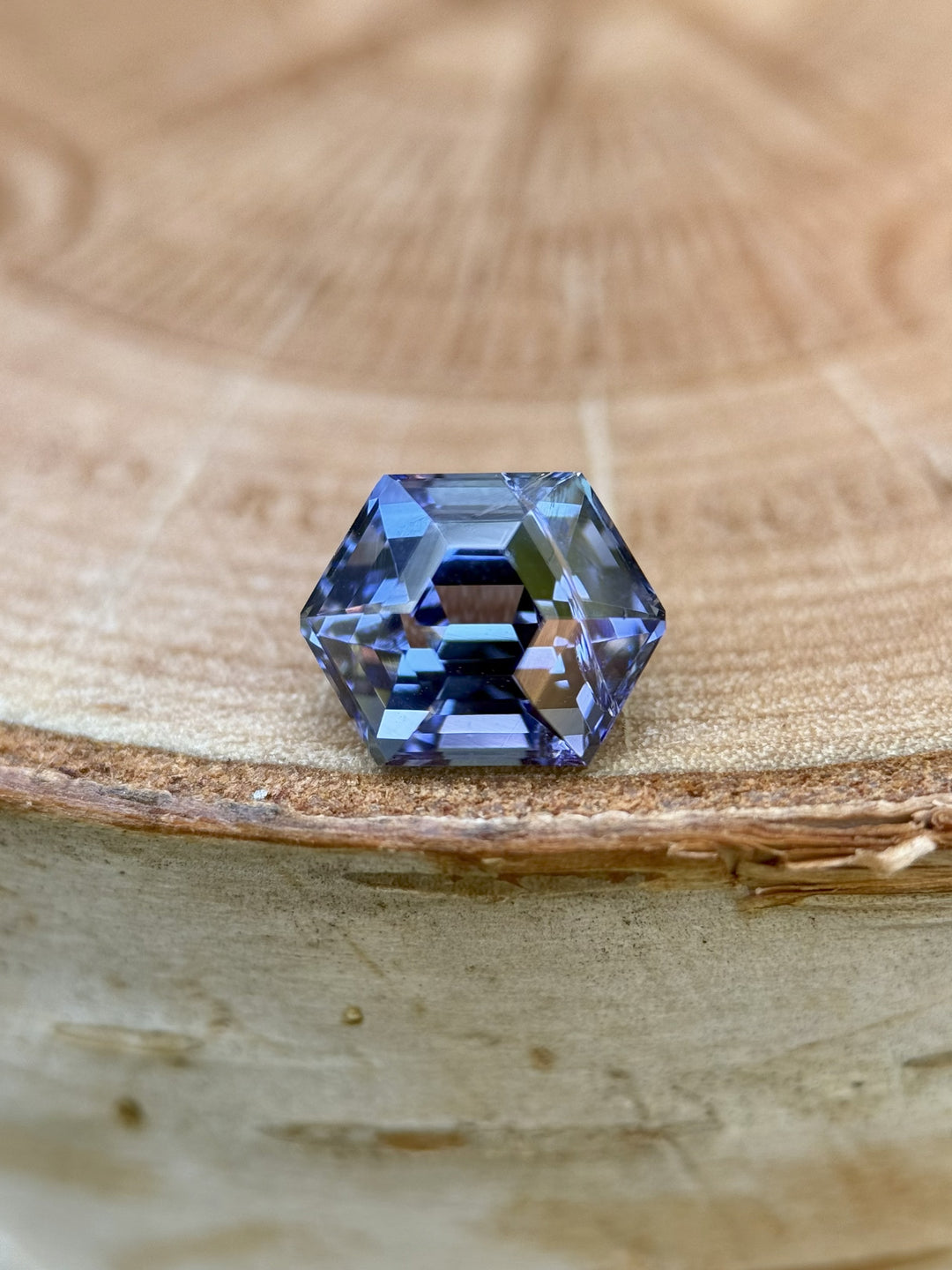 Front-facing close-up of a 2.28 carat unheated Tanzanite gemstone in a geometric step cut hexagon shape, showing rich teal and violet hues, photographed on a wood background.