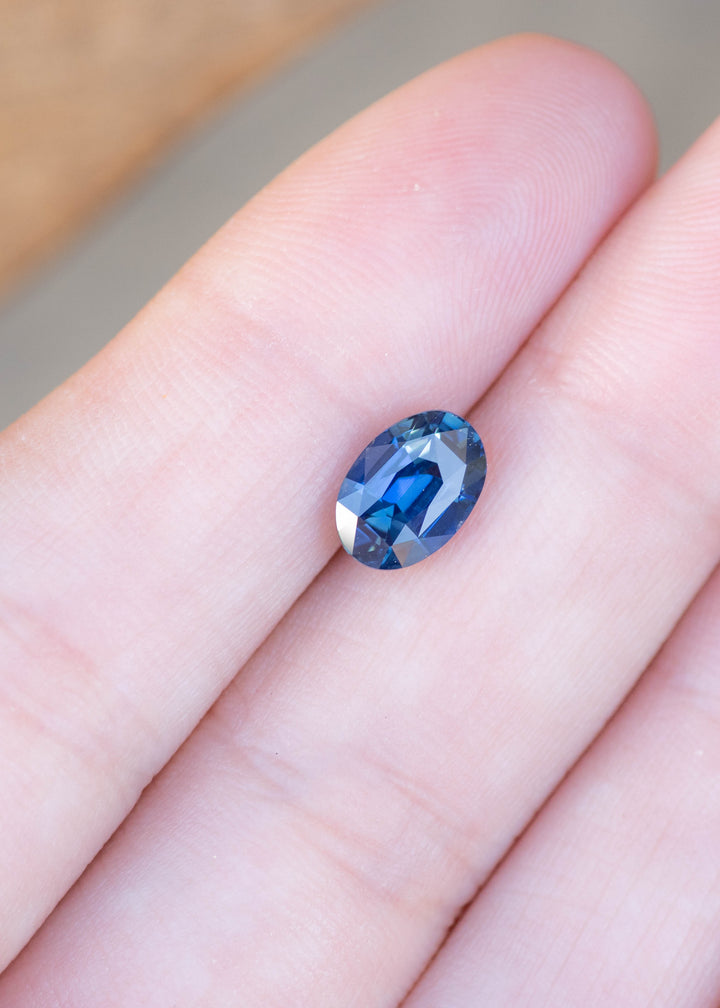2.29ct Deep oceanic blue oval mix cut sapphire held in finger tips under natural light.