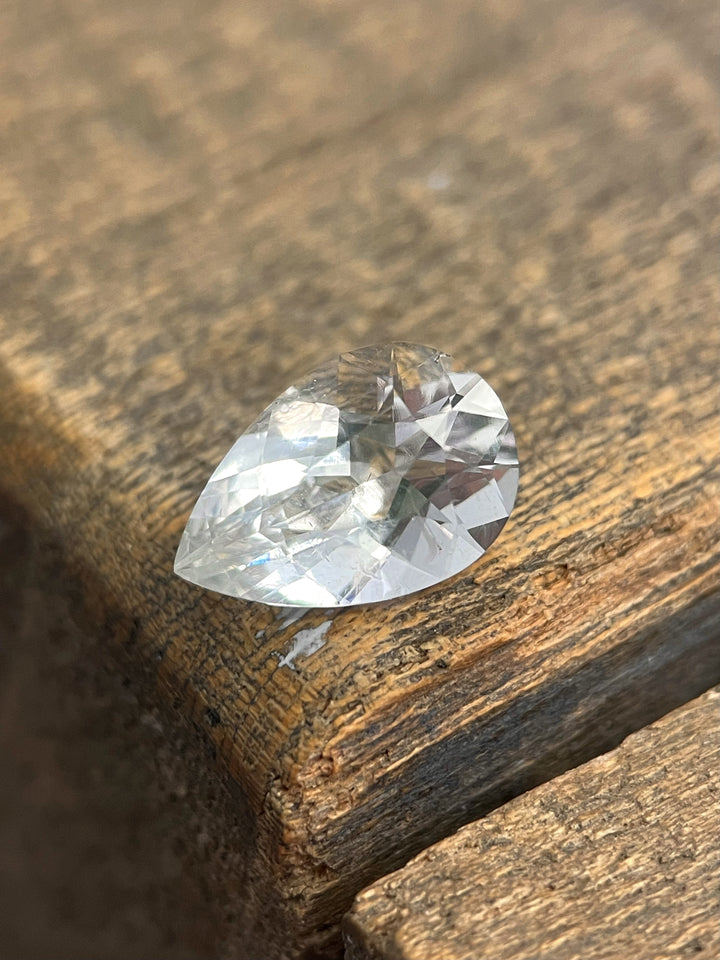 A pear-shaped hyalite opal resting on a wooden surface, displaying its high clarity and light-reflecting facets.