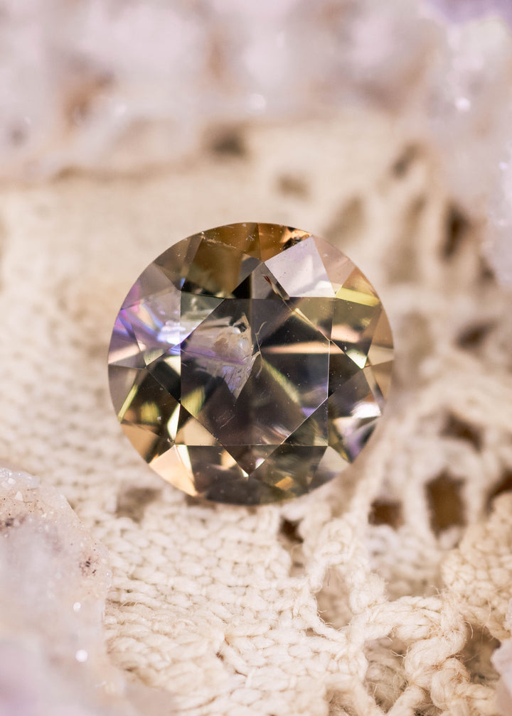 2.33 carat untreated Tanzanite photographed on textured fabric, showing teal, green, purple, and golden yellow colors in an antique style round transitional brilliant cut from Tanzania