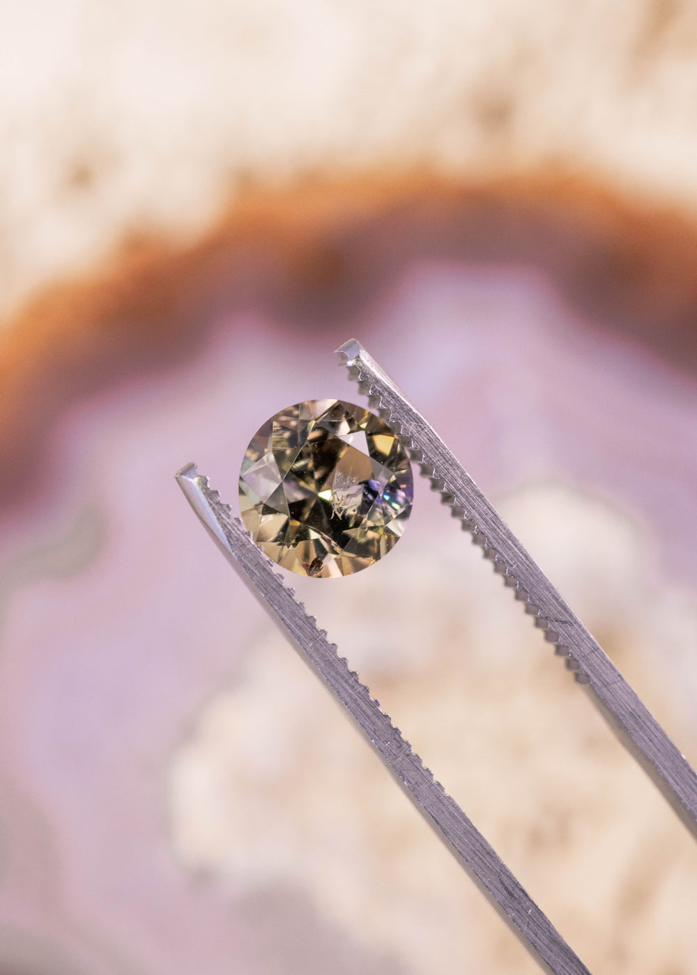 2.33ct Tanzanite held in gem tweezers, highlighting antique round transitional brilliant cut facets and mixed teal, green, purple, and golden yellow hues from Merelani Hills, Tanzania