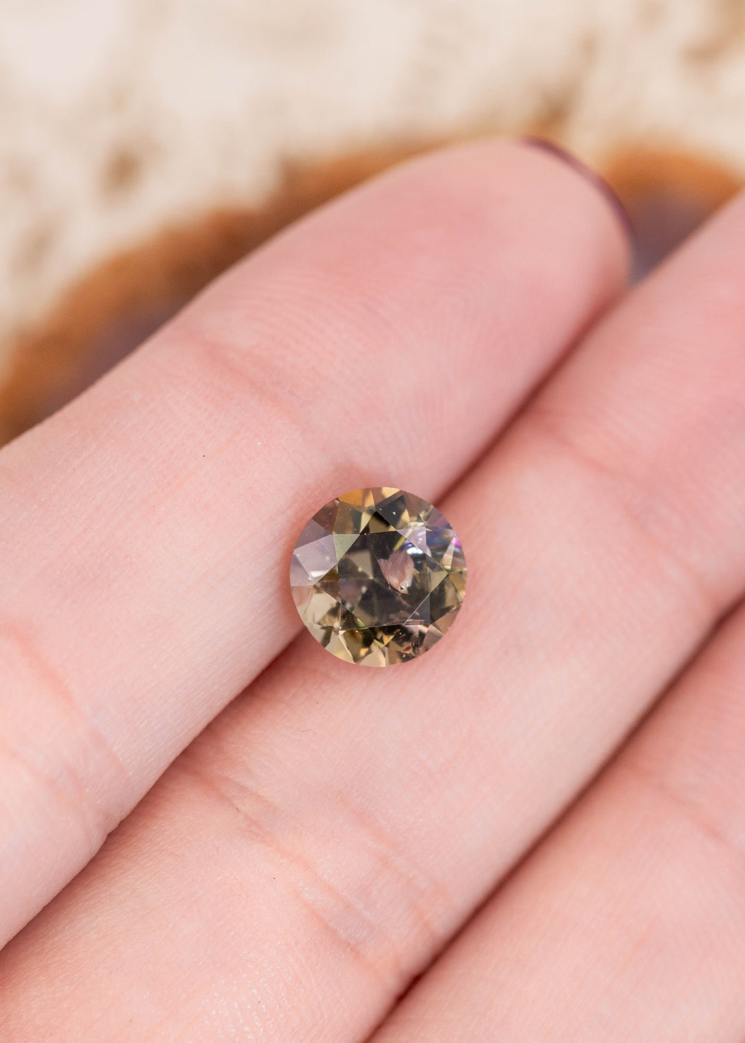 2.33 carat Tanzanite resting on fingertip to show scale and brilliance, featuring an antique style round transitional brilliant cut with teal, green, purple, and golden yellow tones