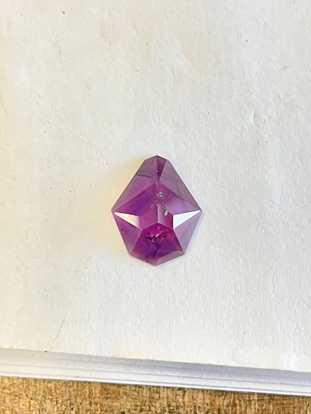Close-up of a 2.38-carat mulberry purple sapphire on a white surface, featuring a custom shield rose cut, sourced from the Umba River, Tanzania, priced at $1,547.