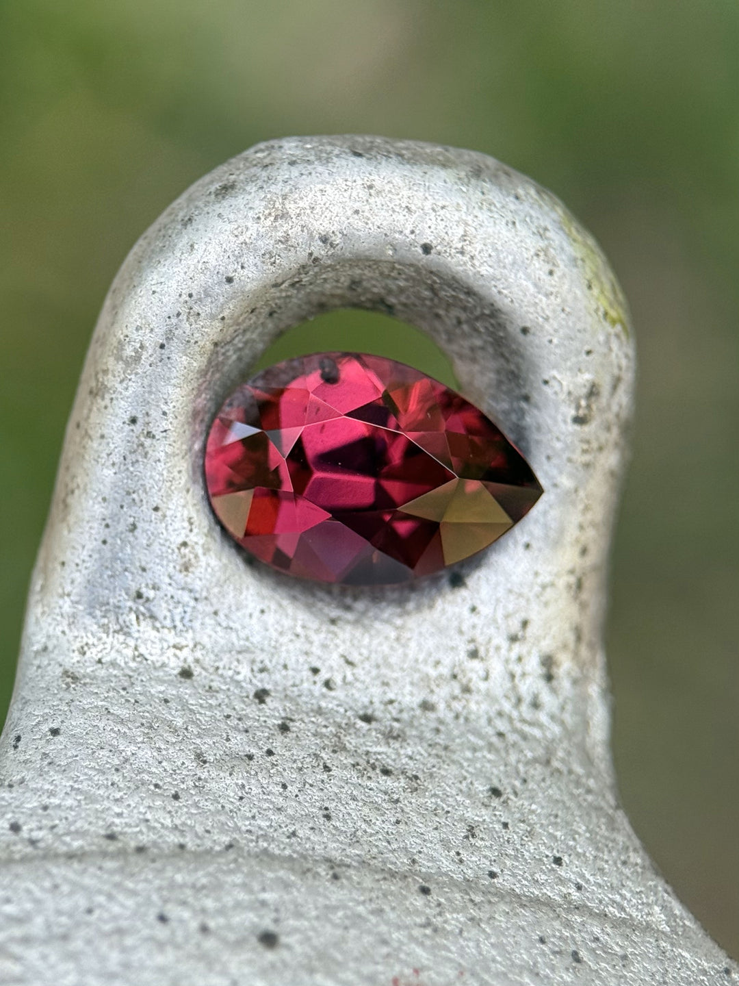 Garnet nestled on textured metal, revealing deep raspberry hues and symmetrical brilliance in poval shape