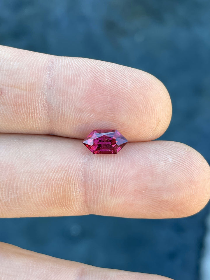 Close-up of a 2.40 carat garnet gemstone from Kenya with a custom geometric hexagon cut, featuring vibrant red and purple hues and natural untreated clarity.