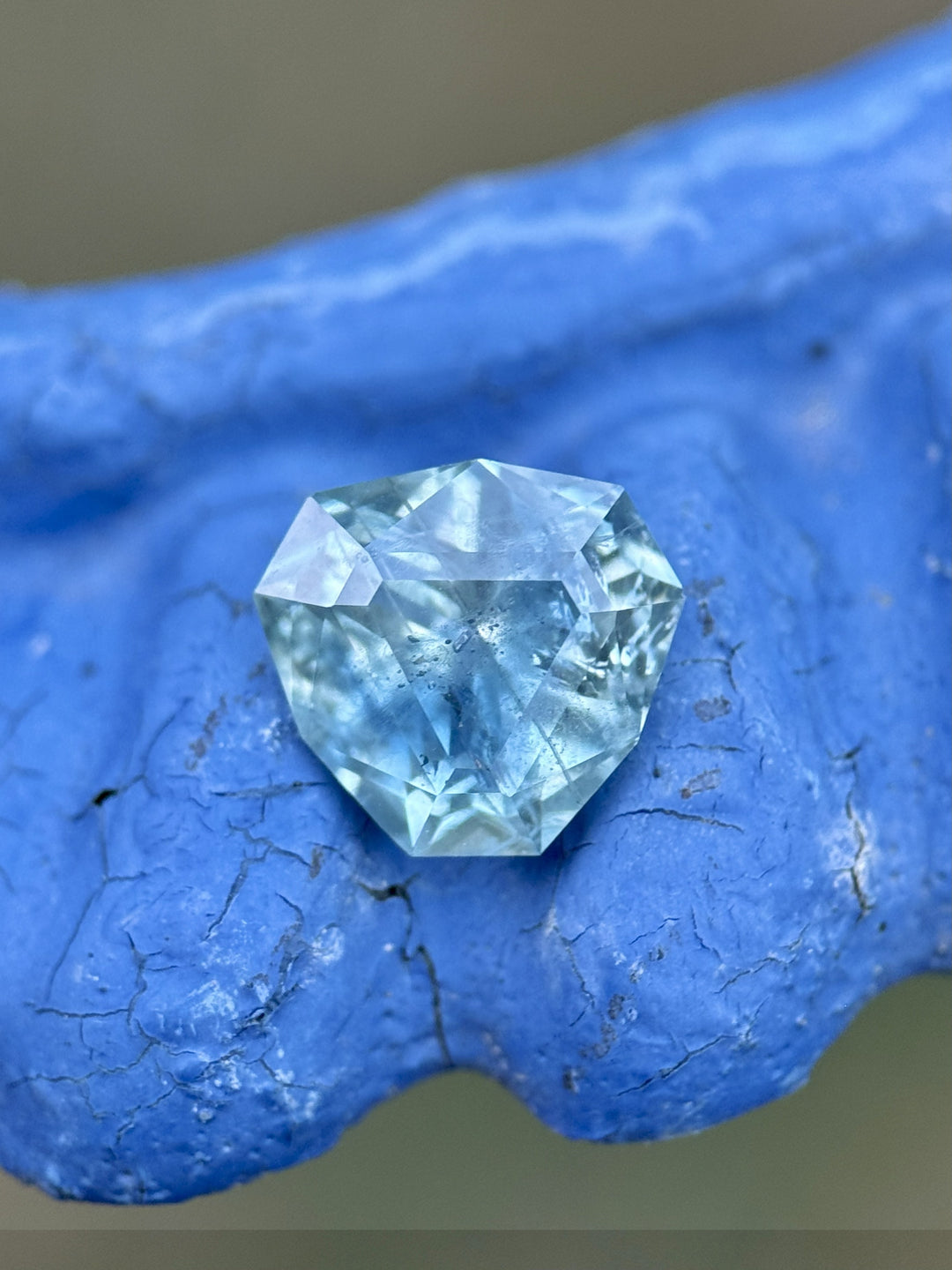 Macro view of heated 2.41ct Montana sapphire resting on blue textured surface, displaying its intricate trillion cut.