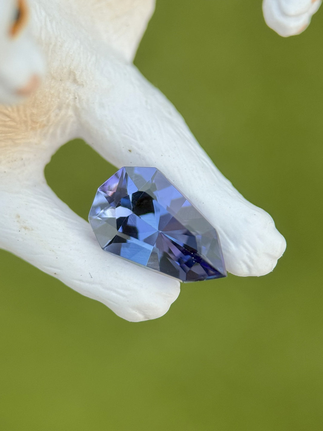 2.42 carat tanzanite with rich blue, purple, and green mermaid hues resting on a white ceramic sculpture, highlighting its custom elongated shield mix cut and natural brilliance from Merelani Hills, Tanzania.