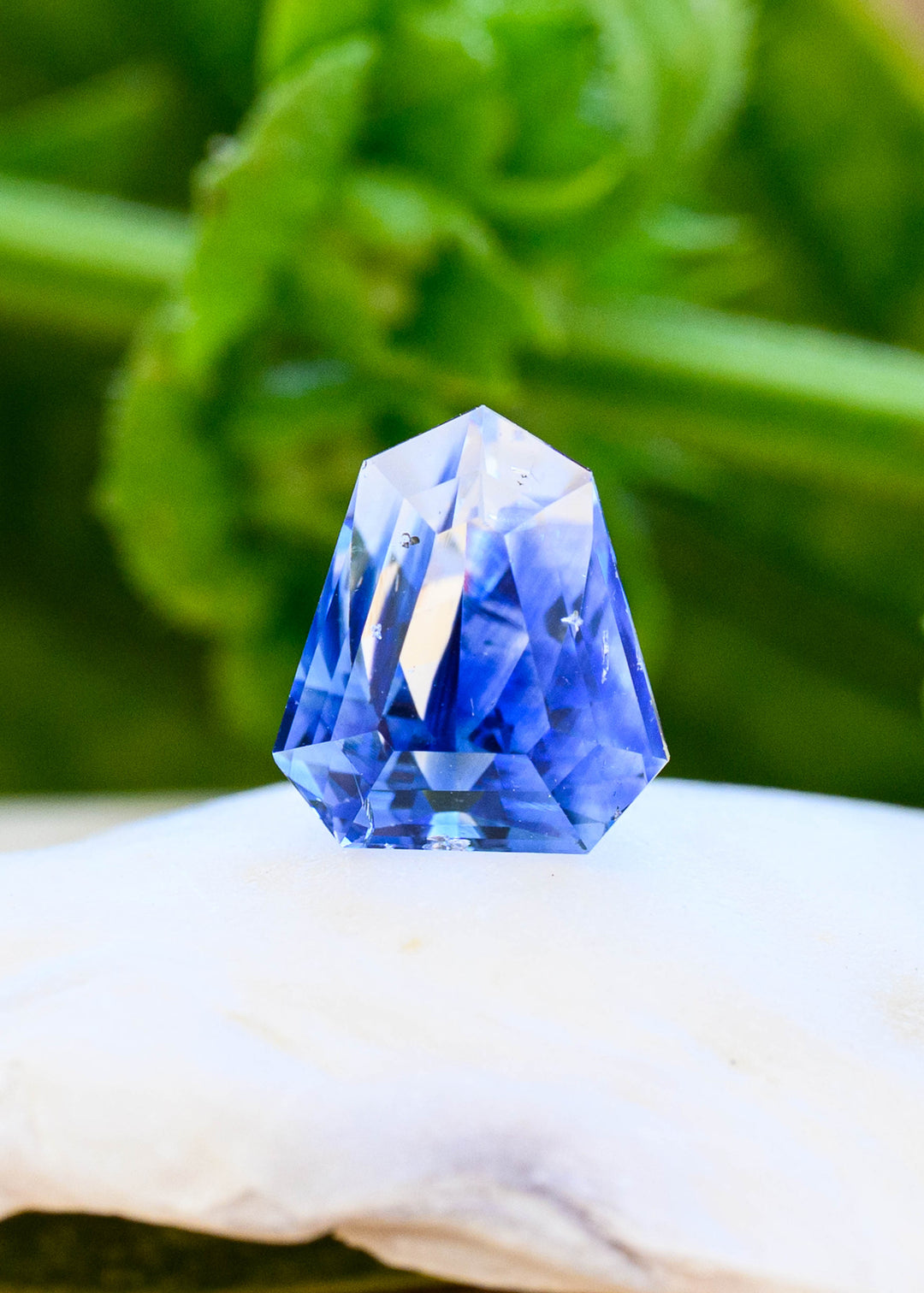 2.42 carat blue and colorless parti sapphire standing on a white surface, showing its angular geometric shield shape, blue color zoning and visible natural inclusions.
