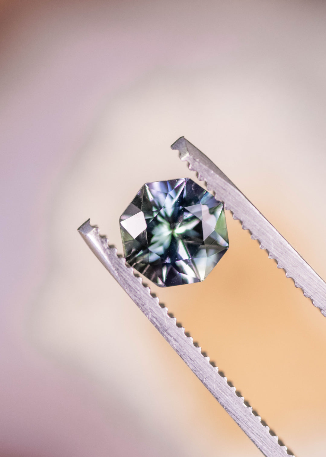 2.45 carat gray lavender blue Tanzanite modified mix brilliant oval held in tweezers, untreated Merelani Hills Arusha Tanzania gemstone displaying clarity, sparkle and precision faceting for fine custom jewelry design