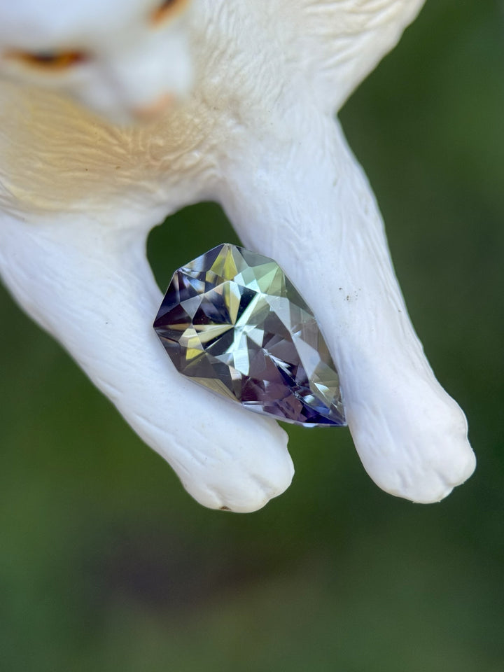 2.46-carat Tanzanite gemstone with mermaid, yellow, and teal hues resting on a white cat figurine – custom geometric pear shape from Merelani Hills, Tanzania