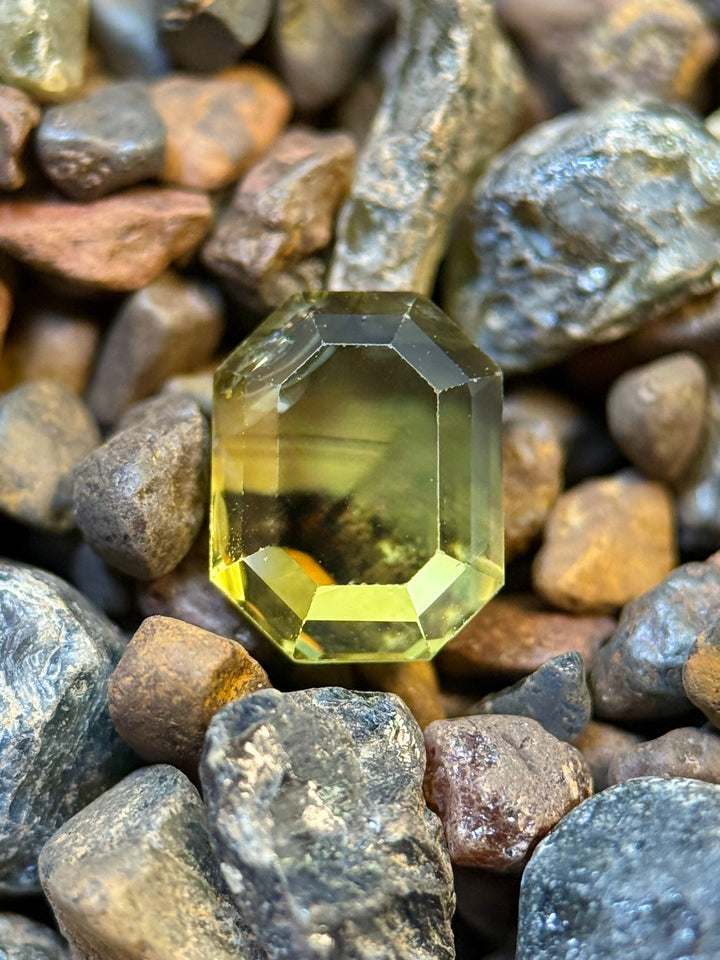 Antique emerald cut loose sapphire resting on rough sapphires showing off vibrant parti coloring and windowing