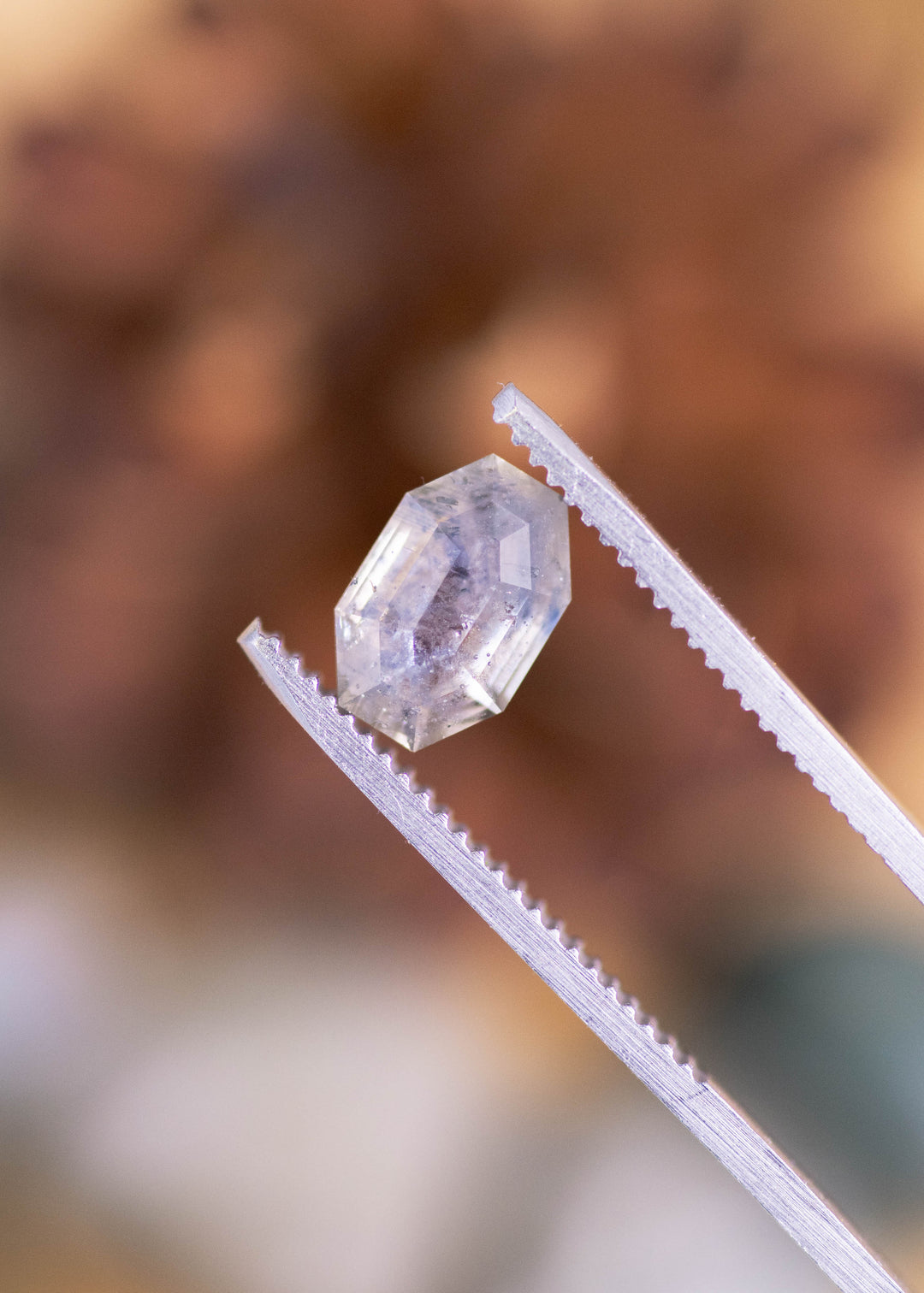 Loose 2.40 carat heated gray purple Montana sapphire held in tweezers, displaying its octagonal tablet cut and architectural facet pattern.