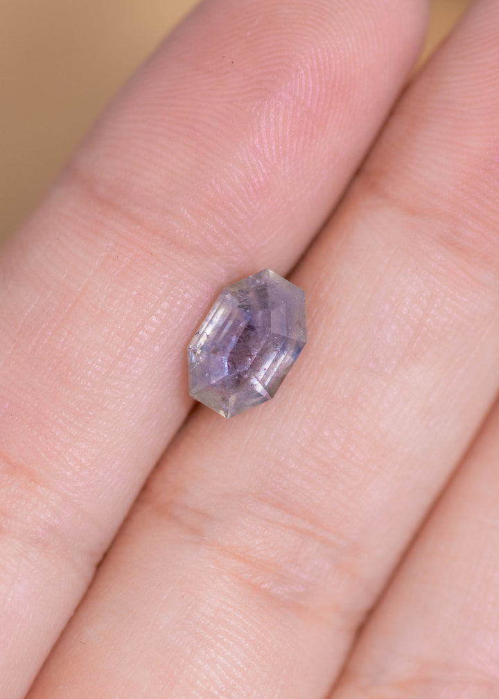 Loose 2.40 carat gray purple sapphire resting on fingertips, highlighting the geometric tablet cut and subtle lavender undertones.