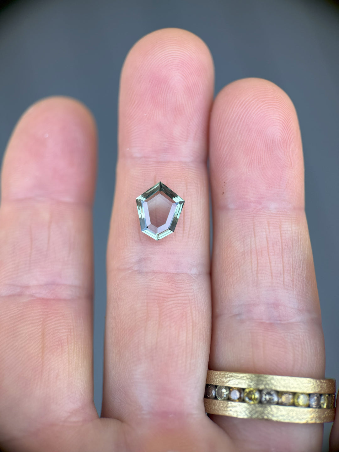 2.50 carat Montana sapphire in custom shield cut showing color change, displayed on hand for scale