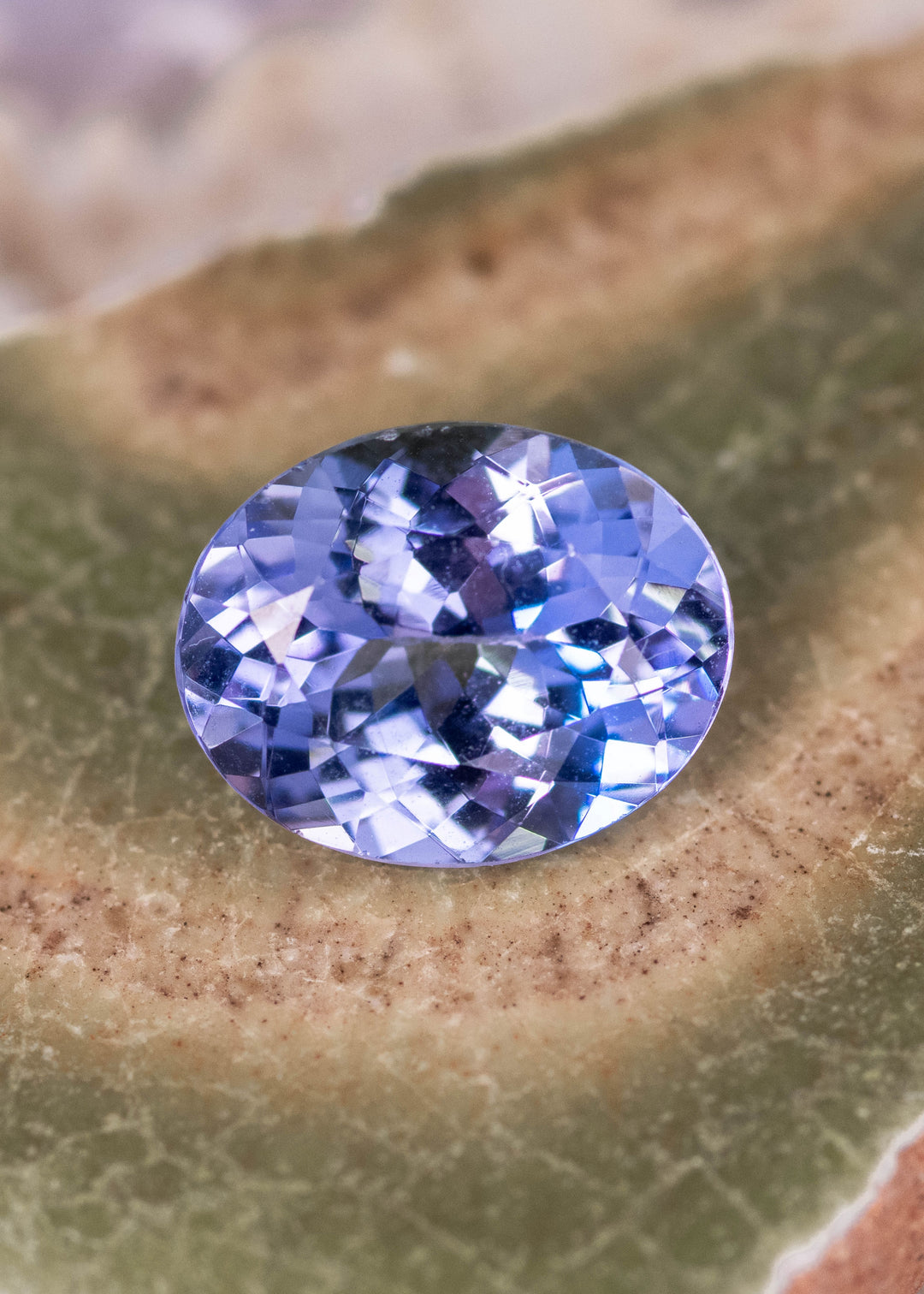 Heated 2.50 carat Tanzanite custom oval mix brilliant cut on display surface showing powder blue violet brilliance and precise faceting
