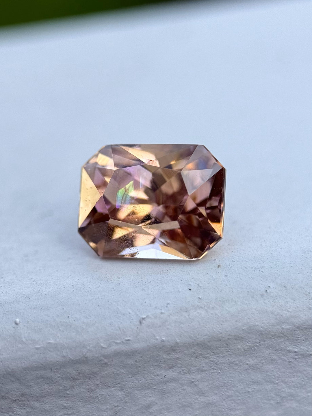 Close-up of a 2.51 carat Tanzanite resting on a ledge, showing its radiant mix of champagne, peach, lavender, and orange hues in a custom modified radiant cut.
