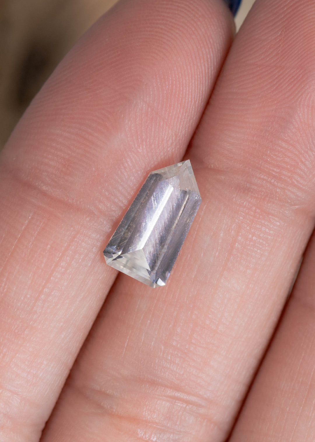 Loose 2.51ct light seafoam sapphire from Sri Lanka shown on a fingertip for scale, with the custom shield step cut reflecting bright, clean lines and a soft blue-green tint.