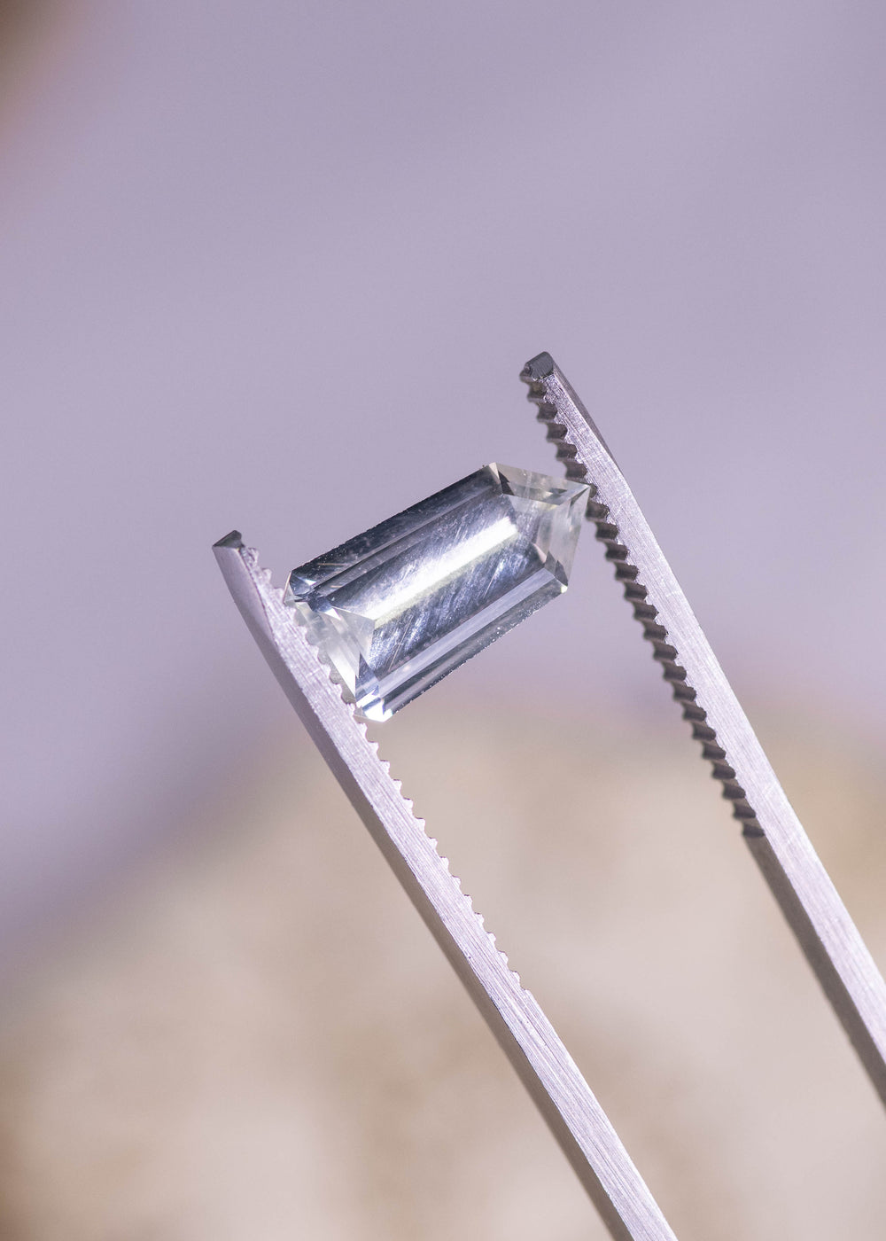 Loose light seafoam no-heat sapphire from Sri Lanka held in jeweler’s tweezers, turned to show the custom shield step cut profile and long step facets flashing in the light.