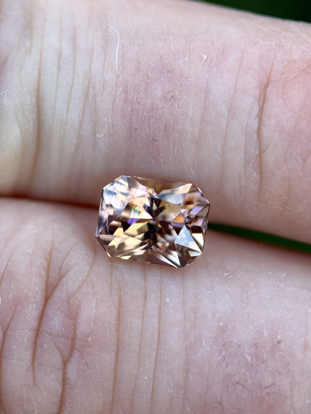 Tanzanite displayed across fingers, revealing a symphony of colors from purple to peach and orange in a beautifully faceted radiant cut.