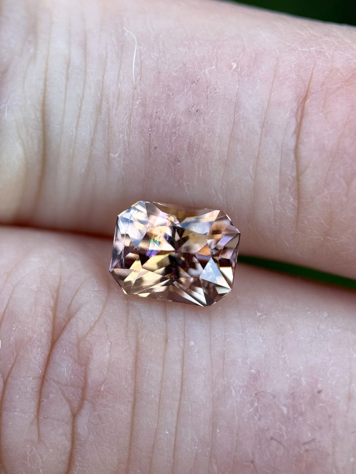 Tanzanite displayed across fingers, revealing a symphony of colors from purple to peach and orange in a beautifully faceted radiant cut.
