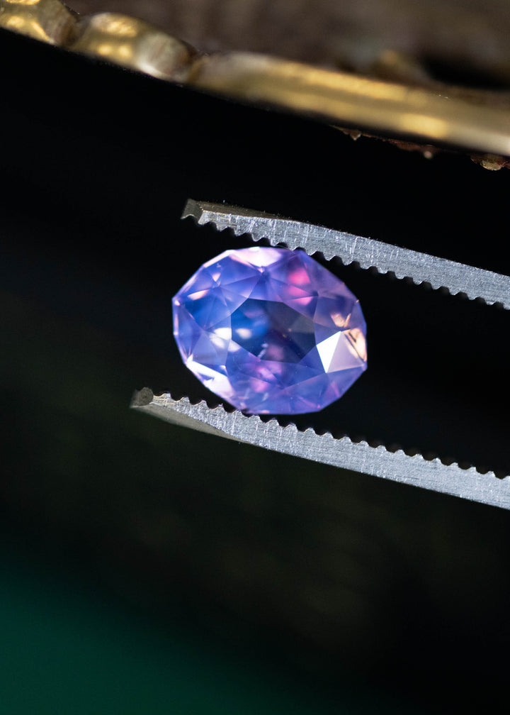 Loose unheated opalescent purple pink sapphire held in tweezers, highlighting crisp facet symmetry and soft lavender rose color zoning.