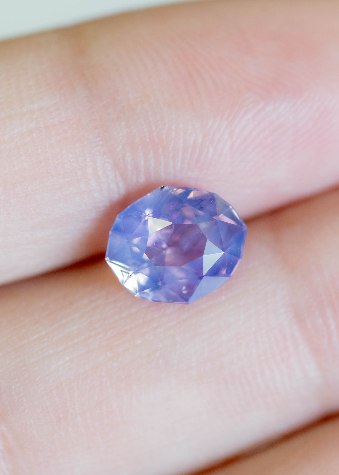 Loose 2.52 carat purple pink sapphire resting on fingertips, revealing shifting rose and violet tones across the precision oval mix cut.