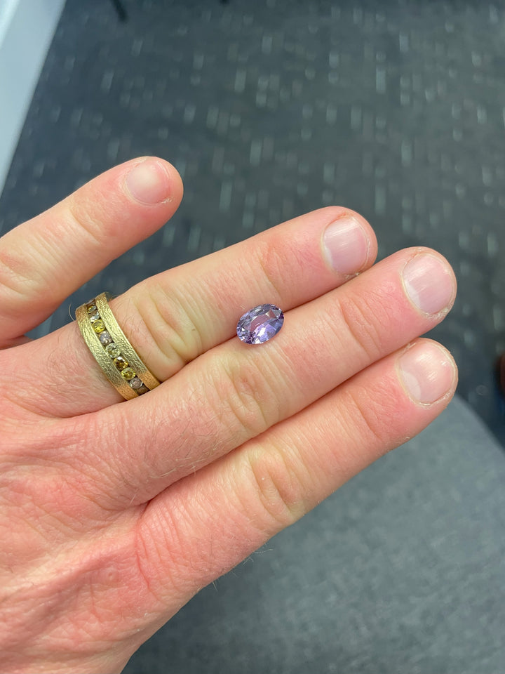 A beautiful purple sapphire weighing 2.56 carats in an oval cut, shown against a natural green background, emphasizing its untreated brilliance.