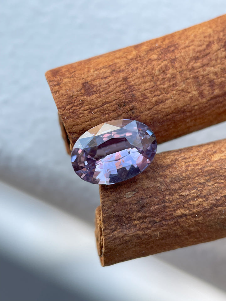 A stunning 2.56 carat purple sapphire in a mix brilliant oval cut, sourced from Sri Lanka, untreated, displayed on a natural cinnamon backdrop.