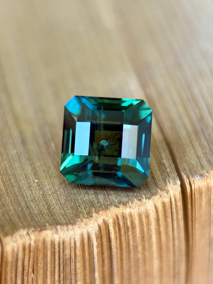 2.56 carat deep lagoon teal green sapphire shown face-up, displaying crisp Asscher cut step facets and rich oceanic color from Garba Tula, Kenya.