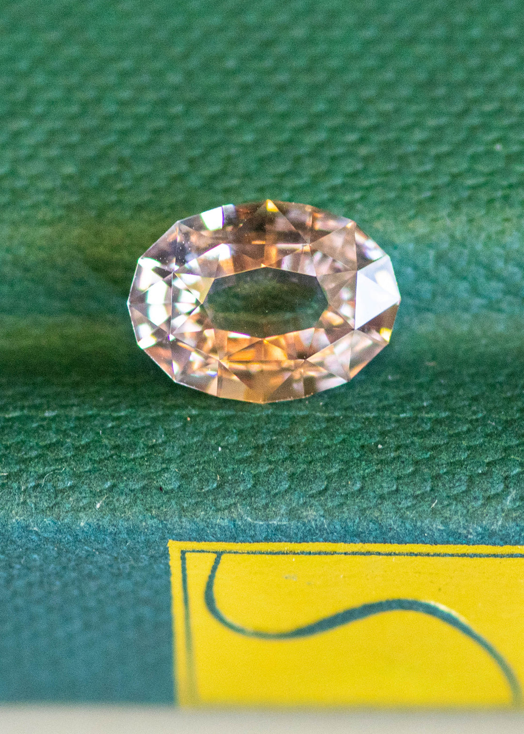 2.56ct blush peach pink antique style oval cut sapphire from Madagascar resting on a textured green book cover.
