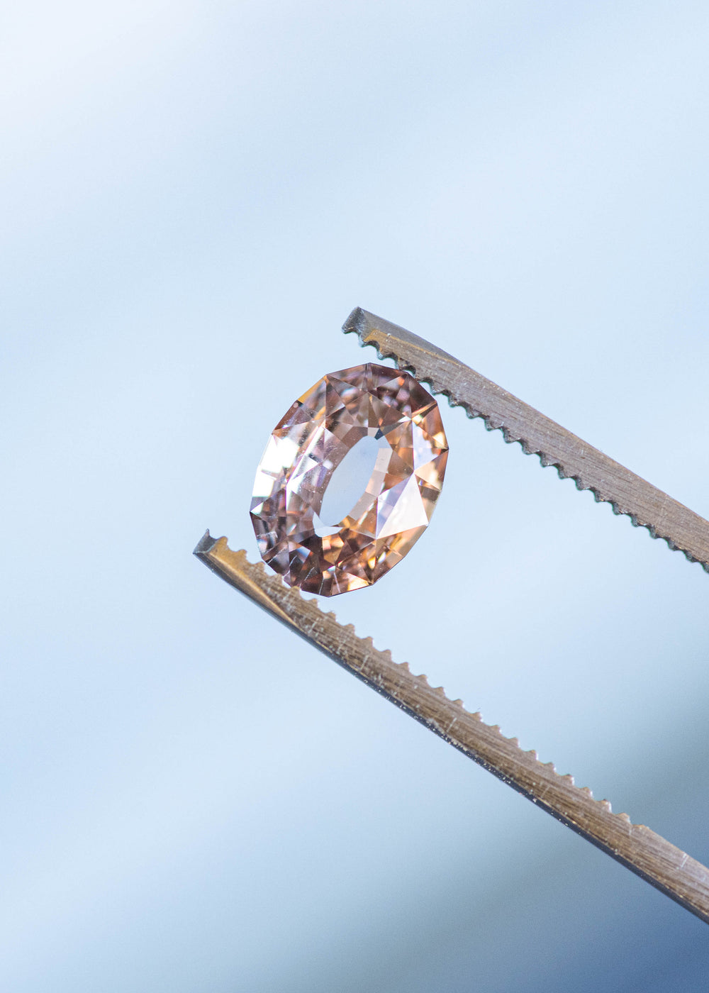 2.56ct blush peach pink antique style oval cut sapphire from Madagascar held in gem tweezers under natural light.