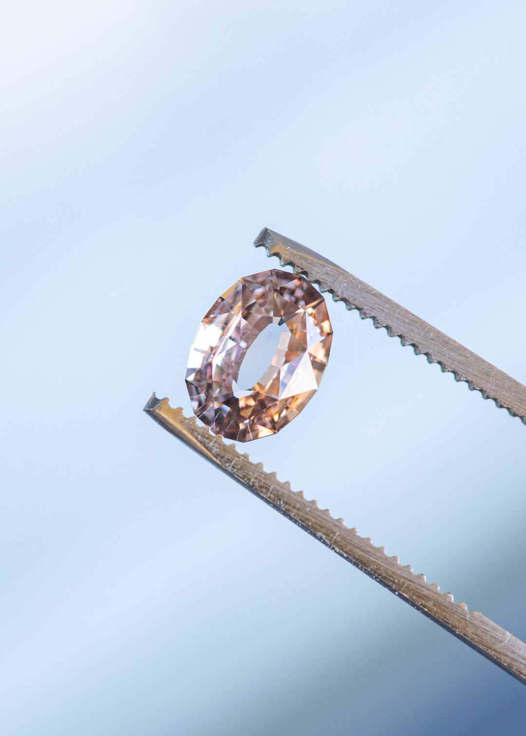 2.56ct blush peach pink antique style oval cut sapphire from Madagascar held in gem tweezers under natural light.