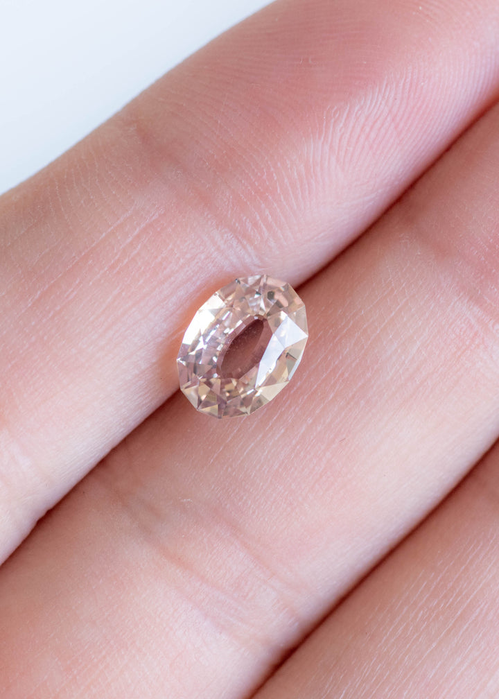 2.56ct blush peach pink antique style oval cut sapphire from Madagascar resting on finger tips showing scale and color.